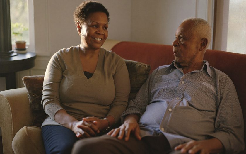 An adult daughter sitting with her elderly father at home